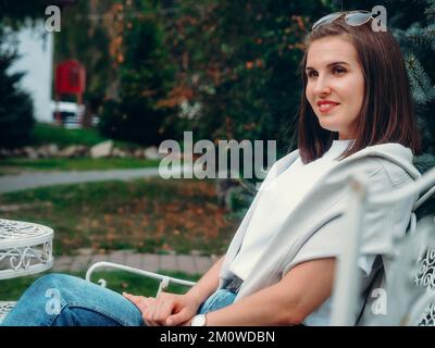 Belle femme caucasienne est assise sur le banc de parc et regarde loin. Portrait d'une fille de 30 ans.. Banque D'Images