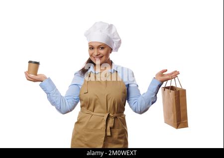 Femme adorable serveuse barman, confiseur portant un chapeau de chef et un tablier, avec une tasse de carton de thé chaud à emporter ou de café Banque D'Images