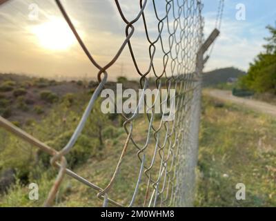 la clôture en fer et le fil barbelé sont parallèles à la route de terre. coucher de soleil dans la campagne. mise au point sélective sur le mur de clôture. Banque D'Images