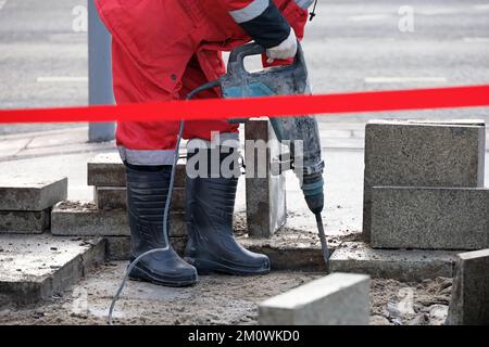 Un ouvrier répare la surface de la route avec un marteau à inertie. Travaux de construction, pose de pavés en ville Banque D'Images