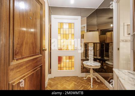 Hall d'entrée d'une maison avec porte d'accès blindée, murs couverts de miroirs, table circulaire avec dessus en marbre et lampe en pierre ethnique. Banque D'Images