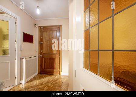 Hall d'entrée d'une maison avec porte d'accès blindée, portes en bois blanc avec verre au plomb, parquet en chêne et couverture de radiateur en maille Banque D'Images