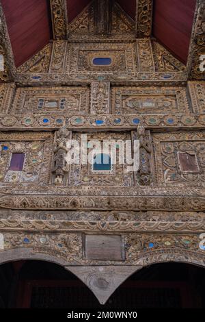 Vue rapprochée d'un décor de pignon en bois avec incrustation en verre de l'ancienne salle d'ordination de style Lanna au temple bouddhiste Wat Bupfaram, Chiang Mai, Thaïlande Banque D'Images