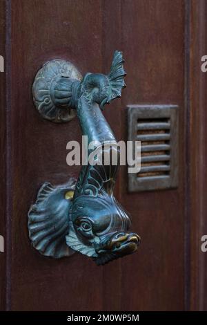 Vue rapprochée de poissons mythologiques en forme de bronze vintage poignée de porte isolée sur la belle ancienne porte en bois marron, Montpellier, France Banque D'Images