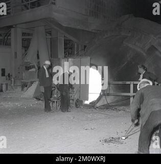 1950s, historique, aciéries, deux aciéries dans un four, debout derrière une garde de protection, l'une tenant une barre d'acier dans le four, Abbey Works, Port Talbot, pays de Galles du Sud, Royaume-Uni. Banque D'Images