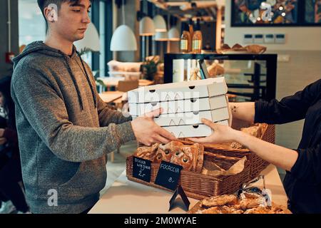 Jeune homme recevant de la pizza fraîche dans des boîtes à emporter de la femme employée dans une pizzeria et un café-restaurant. Homme de récupérer sa commande de la pizzeria pendant Banque D'Images