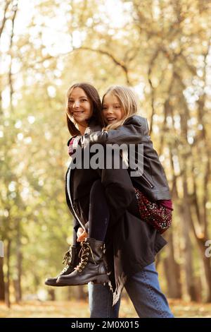 Famille de mère gaie, ludique et positive tenant sa fille à l'arrière, marchant dans la forêt d'automne dorée. Adoption par les enfants Banque D'Images