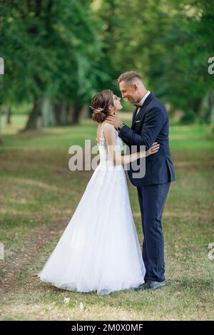 Jeune homme marié mettant les bras autour du cou de jeune femme étonnante mariée, embrassant, rencontrer des yeux, embrassant. Mariage, amour. Banque D'Images