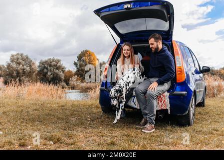 Un jeune couple s'amuse avec un chien dalmate en plein air. Banque D'Images