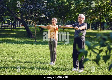 Les plus âgés de 60 conjoints portent des vêtements de sport faire des exercices de mains, l'entraînement des armes à l'extérieur dans le parc d'été le matin à l'aide de élastiques de résistance. lif sain Banque D'Images