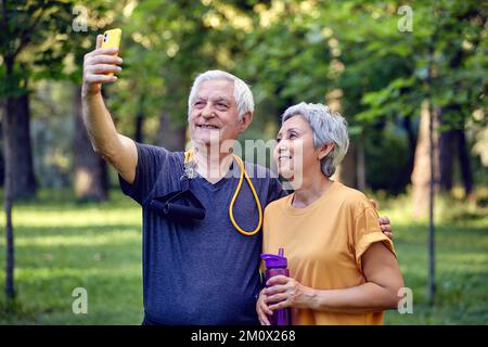 Vieux couple sportif regardant la caméra de smartphone prendre des photos de selfie Profitez de l'utilisation moderne de la technologie sans fil tout en flânant dans les vêtements de sport dans le parc d'été. Carétre Banque D'Images