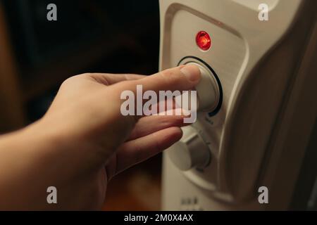 Homme réglant la température sur le chauffage électrique à l'huile à la maison. Hiver froid, concept de crise économique. Banque D'Images