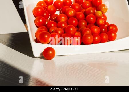 Tomates cerises. Tomates cerises dans une assiette blanche. Lumière intense. Lumière vive et ombre. Banque D'Images