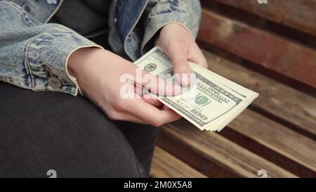 Compter de l'argent dans la rue. Une femme compte une grande quantité de dollars américains assis sur un banc. Banque D'Images