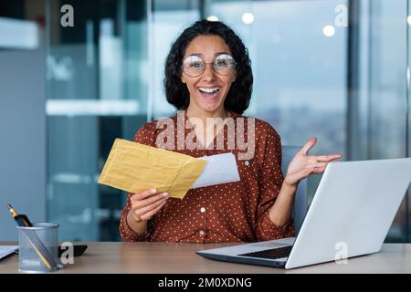 Portrait d'une jeune étudiante latino-américaine. Assise à la table, tenant une lettre avec une enveloppe, elle a reçu un avis sur l'admission à l'université, les résultats des examens. Banque D'Images