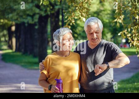 Les couples âgés s'entraîner en été dans le parc porter montre vérifier les données en utilisant l'application se soucier de la santé. Active sportive retraités conjoints style de vie à l'aide de moderne Banque D'Images