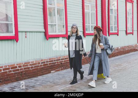 Deux joyeuses touristes souriant et marchant avec des valises dans la rue de la ville en automne ou au printemps - Voyage et concept de vacances Banque D'Images