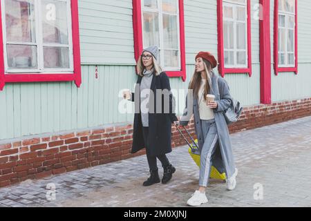 Deux joyeuses touristes souriant et marchant avec des valises dans la rue de la ville en automne ou au printemps - Voyage et concept de vacances Banque D'Images