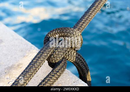 Nœud nautique sur une corde de yacht contre le fond de l'eau sur la jetée. Yacht attaché avec une corde dans le port maritime. Photo de haute qualité Banque D'Images