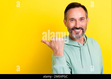 Gros plan photo de sourire gai homme mature âge porter élégant vert Hoodie doigt point vide espace promouvoir produit isolé sur fond jaune Banque D'Images
