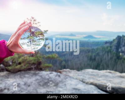 Main tenant la sphère en verre devant la vallée. Vue à travers la lentille de verre à la vallée, jour nuageux Banque D'Images