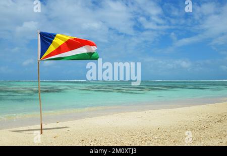 Belle plage de sable tropical Anse Source d'argent avec drapeau des Seychelles sur l'île de la Digue. Banque D'Images