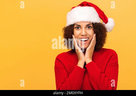 Une femme heureuse et agréablement excitée dans un chapeau de père noël avec une expression faciale surprise sur fond orange Banque D'Images