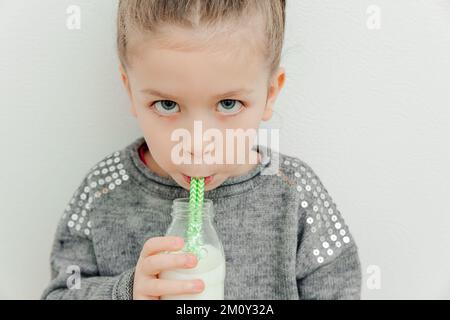 Mignon petite fille élégante avec mode coiffure boire du lait. Fond blanc, prise en studio Banque D'Images