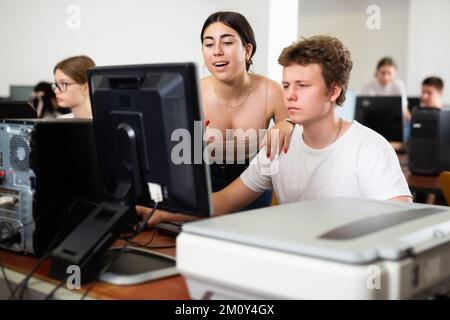 Femme adolescente souriante aidant le camarade de classe masculin pendant qu'il apprend l'informatique dans la classe Banque D'Images