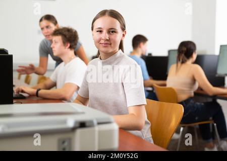 Souriante étudiante utilisant PC et xerox tout en étudiant l'informatique dans la salle de classe Banque D'Images
