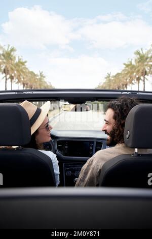 Joyeux couple caucasien en voiture décapotable qui se regarde les uns les autres et souriant par temps ensoleillé. Banque D'Images