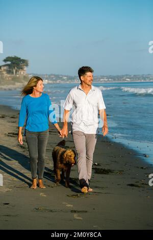 Couple heureux marchant avec leur Labradoodle sur la plage Banque D'Images