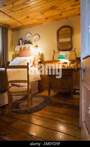 Fauteuil à bascule antique à côté d'un lit simple dans la chambre d'amis à l'intérieur de 1977 réplique construite de l'ancienne maison en rondins Canadiana des années 1800. Banque D'Images