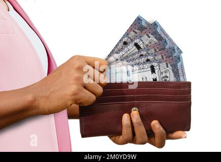 Main féminine équitable tenant le sac à main brun avec des notes de Riyal saoudien, main retirant l'argent du sac à main isolé sur fond blanc Banque D'Images