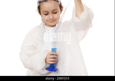 Une petite fille en gros plan remplit la pipette graduée en verre de laboratoire avec une solution chimique bleue provenant d'une éprouvette graduée Banque D'Images