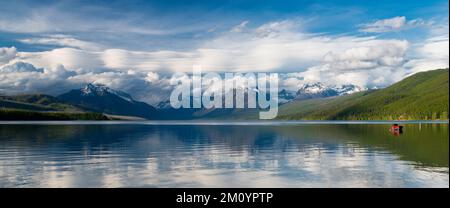 Panorama des sommets enneigés et du bateau rouge sous un ciel spectaculaire, reflété dans les eaux calmes du lac McDonald, parc national des Glaciers, Montana Banque D'Images