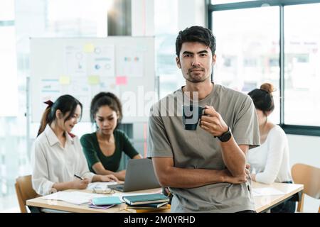 Portrait d'un heureux propriétaire asiatique de petite entreprise posant avec les mains pliées. Un chef d'équipe millénaire souriant, regardant la caméra, les employés qui travaillent Banque D'Images