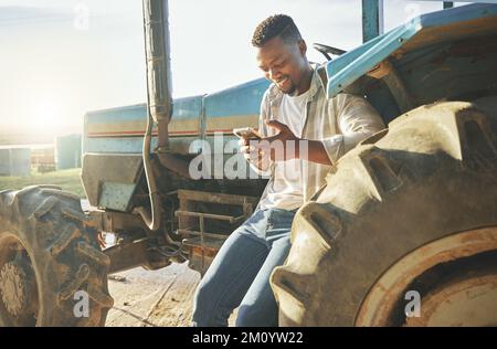 L'information est une ressource précieuse sur une ferme. un jeune agriculteur utilisant un téléphone en se tenant contre un tracteur. Banque D'Images