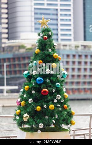 Vue verticale d'un arbre de Noël décoration de célébration d'hiver à l'extérieur contre divers bâtiments commerciaux paysage urbain en arrière-plan. Singapour. Banque D'Images