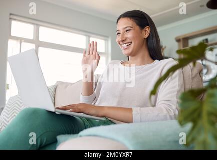 C'est tellement agréable de vous voir... une femme qui agite tout en utilisant son ordinateur portable sur le canapé à la maison. Banque D'Images