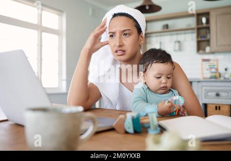 Le temps passe lorsque vous avez un horaire chargé. une femme qui regarde stressée tout en regardant son ordinateur portable et en tenant son bébé sur ses genoux. Banque D'Images