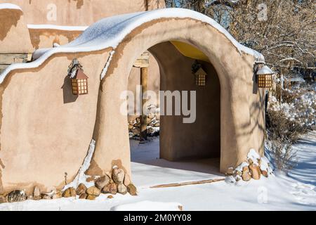 Scène hivernale enneigée d'un mur en adobe recouvert de neige avec une entrée voûtée à Santa Fe, Nouveau-Mexique Banque D'Images