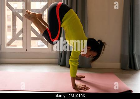 Jeune et forte femme, vêtue de vêtements de sport, exécute des exercices de calisthénie sur le plancher de l'appartement Banque D'Images