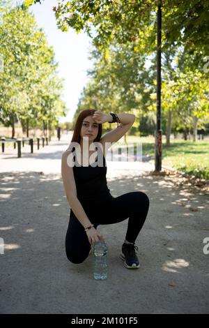 Souriant sportswoman s'étirant les jambes dans le parc par beau temps Banque D'Images