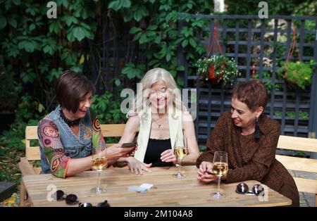 Des amis femelles matures jouent au jeu de carte dans le café, s'amusent, rient et boivent du vin de bakals. Les femmes d'âge moyen loisirs Banque D'Images