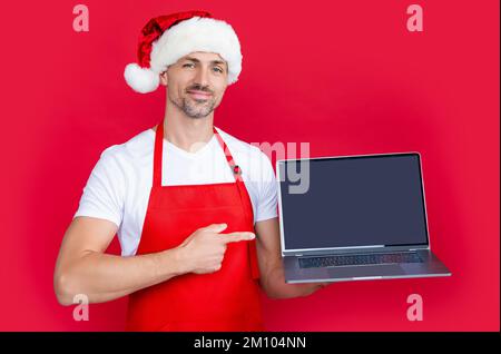 homme mature en chapeau de père noël nouvel an et tablier rouge présentant l'ordinateur portable Banque D'Images