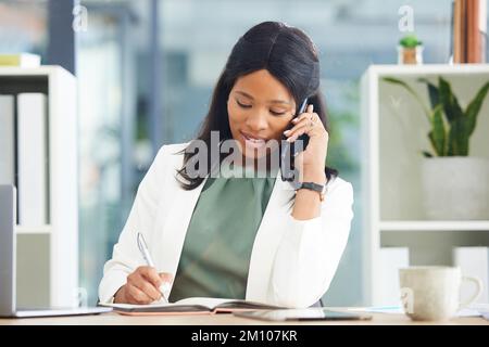 Une femme noire, un appel téléphonique et professionnel tout en écrivant dans un carnet, un journal et un planificateur au bureau. Femme entrepreneur parlant sur smartphone pendant Banque D'Images