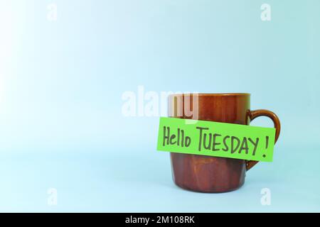 Concept de bienvenue, bonjour et Happy Tuesday. Mise au point sélective d'une tasse à café avec message écrit isolé sur fond bleu. Banque D'Images