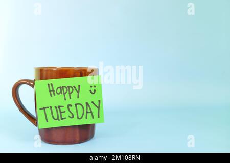 Concept de bienvenue, bonjour et Happy Tuesday. Mise au point sélective d'une tasse à café avec message écrit isolé sur fond bleu. Banque D'Images