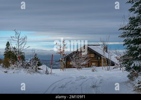 Holzhaus, Ferienhaus am Waldrand auf dem Hügel im ersten Schnee, verschneite Landschaft mit weißen Wiesen und Bäumen. Avent und Weihnachtszeit Ferien Banque D'Images